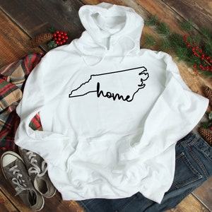May include: White hooded sweatshirt with a black outline of the state of North Carolina and the word "home" written in cursive.