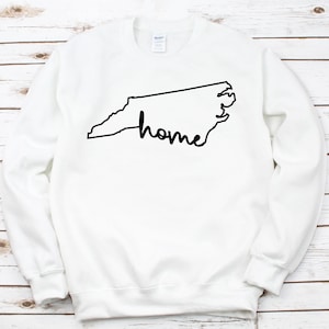 May include: White sweatshirt with a black outline of the state of North Carolina and the word "home" written inside the outline.