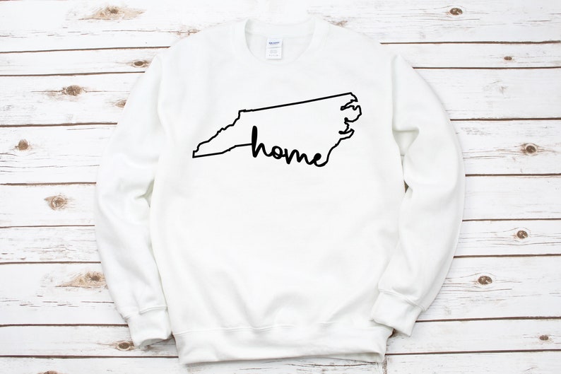 May include: White sweatshirt with a black outline of the state of North Carolina and the word "home" written inside the outline.