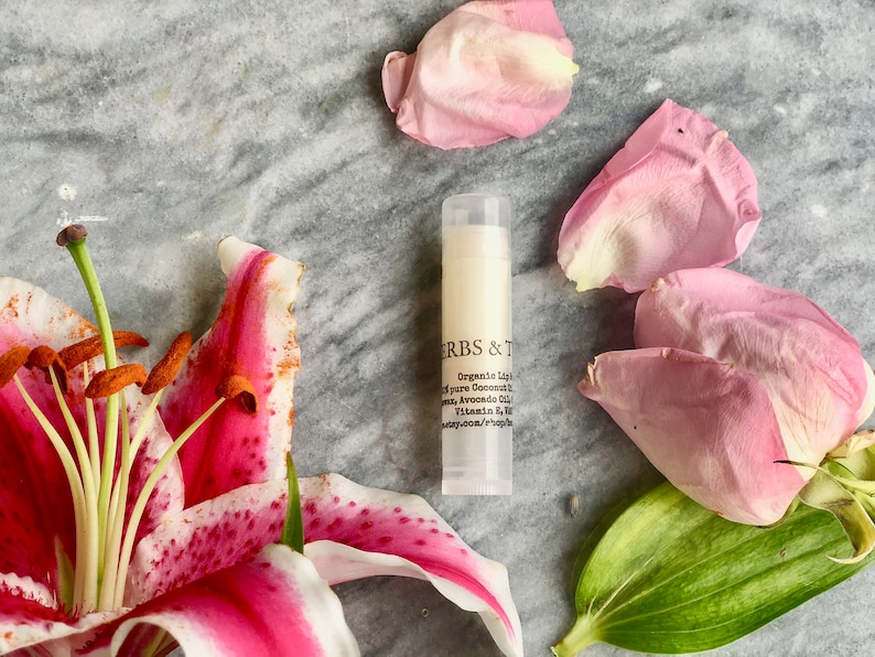 May include: A white tube of lip balm with black text that reads "HERBS & T Organic Lip Balm with pure Coconut Oil, Shea, Avocado Oil, Vitamin E & B. herbsandtea.com/shop"