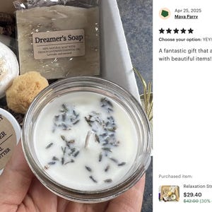 May include: A gift box containing a candle, soap, bath bomb, body butter, and a natural sponge. The candle is in a glass jar and has lavender buds. The soap is labeled "Dreamer's Soap". The body butter is labeled "Oatmeal & Honey Lavender Body Butter".