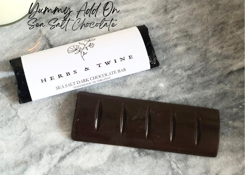 May include: A dark chocolate bar with sea salt, wrapped in black and white packaging with the text "HERBS & TWINE SEA SALT DARK CHOCOLATE BAR HANDMADE IN VIRGINIA".