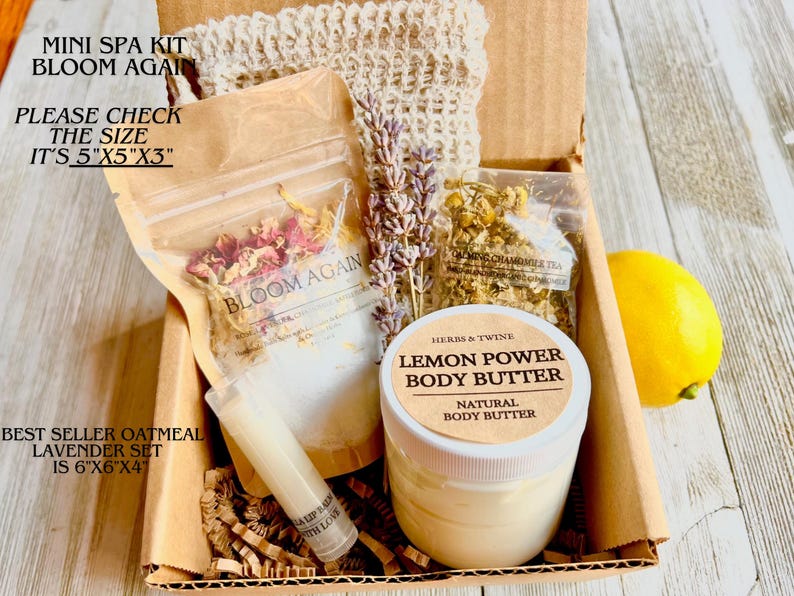May include: A mini spa kit in a cardboard box. The kit includes a jar of Lemon Power Body Butter, a lip balm, dried lavender, and chamomile tea. The box is labeled "Bloom Again" and measures 5"x5"x3".