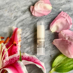 May include: A white tube of lip balm with black text that reads "HERBS & T Organic Lip Balm with pure Coconut Oil, Shea, Avocado Oil, Vitamin E & B. herbsandtea.com/shop"