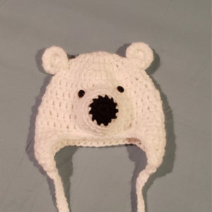 May include: White crocheted polar bear hat with black eyes and nose. The hat has two long ties that can be tied under the chin.