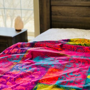 May include: A colorful bedspread with a patchwork design featuring bright pink, yellow, blue, and orange hues. The bedspread has a floral pattern and is made of a soft, comfortable fabric.