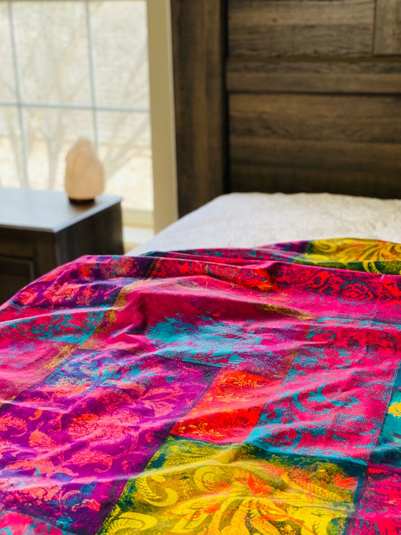 May include: A colorful bedspread with a patchwork design featuring bright pink, yellow, blue, and orange hues. The bedspread has a floral pattern and is made of a soft, comfortable fabric.