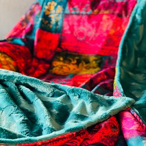 May include: A teal blue plush blanket with a patterned underside featuring a patchwork of red, pink, yellow, and blue floral designs.