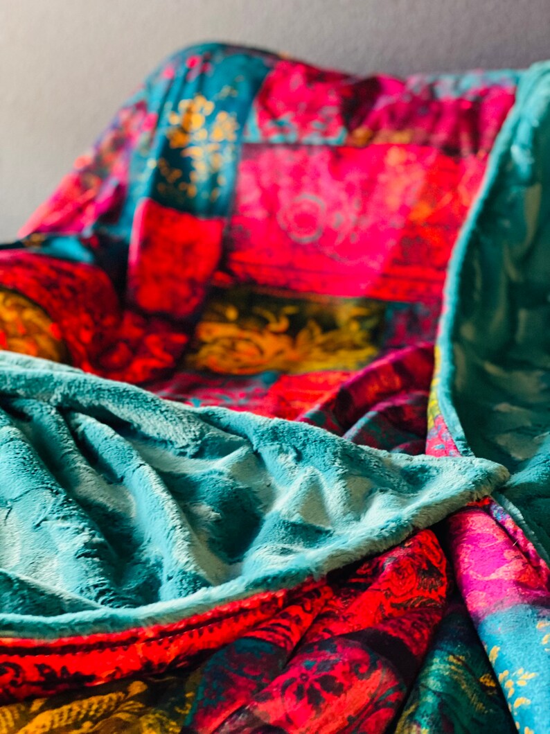 May include: A teal blue plush blanket with a patterned underside featuring a patchwork of red, pink, yellow, and blue floral designs.