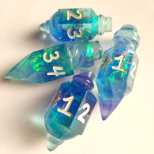 May include: Five blue and teal resin dice, each shaped like a potion bottle. The dice have white numbers and iridescent inclusions. The numbers visible are 1, 2, 3, and 4. The dice are on a white background.