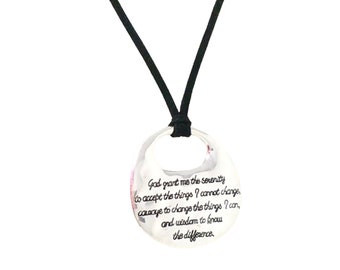 May include: A silver-colored pendant necklace with a black cord. The pendant is a circular shape with an open center and features an engraved inspirational quote. The text reads, "God grant me the serenity to accept the things I cannot change..."