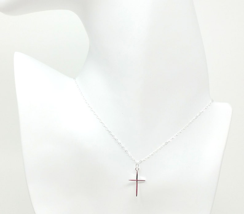 May include: A silver chain necklace with a small silver cross pendant.