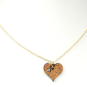 May include: A gold chain necklace with a wooden heart pendant. The heart is made of puzzle pieces, with one piece missing.