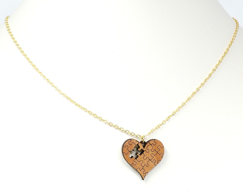 May include: A gold chain necklace with a wooden heart pendant. The heart is made of puzzle pieces, with one piece missing.