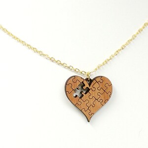 May include: A gold chain necklace with a wooden heart pendant. The heart is made up of puzzle pieces, with one piece missing.