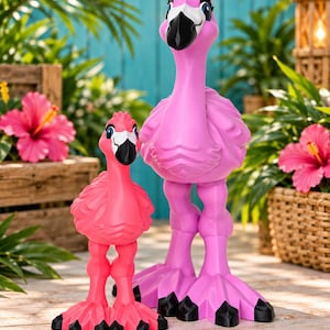 Puede incluir: Dos figuras de flamencos estilizadas colocadas una al lado de la otra. La figura más pequeña es de color rosa brillante, mientras que la más grande es de un tono rosa más claro. Ambas tienen ojos grandes con pestañas largas y picos negros.