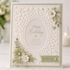 Op de afbeelding: Een witte verjaardagskaart met reliëfhartjes en bloemaccenten. De kaart heeft de tekst "Happy Birthday" en "For You". Het ontwerp bevat een lichtgroene rand en decoratieve elementen.
