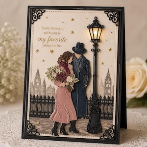 Puede incluir: Tarjeta de felicitación romántica con una pareja bajo una farola con el texto "Every moment with you is my favorite place to be". La tarjeta tiene un marco negro con esquinas decorativas, un fondo de paisaje urbano y estrellas doradas.