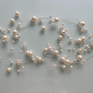 Pode incluir: Uma guirlanda de pérolas brancas com fio prateado. A guirlanda é feita de pérolas falsas de tamanhos diferentes.