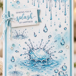 May include: A rectangular greeting card featuring a watercolour-style illustration of blue water droplets and splashes. A white rectangular tag with the text "SENDING YOU A splash OF HAPPINESS" is attached with blue and white twine, accented by clear gems.