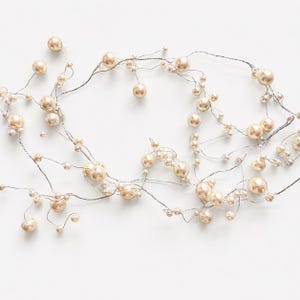 Può includere: Una delicata ghirlanda di perle finte di varie dimensioni, infilate su un filo sottile color argento. Le perle sono di un morbido beige crema, creando un'estetica sottile ed elegante. Ideale per uso nuziale o decorativo.