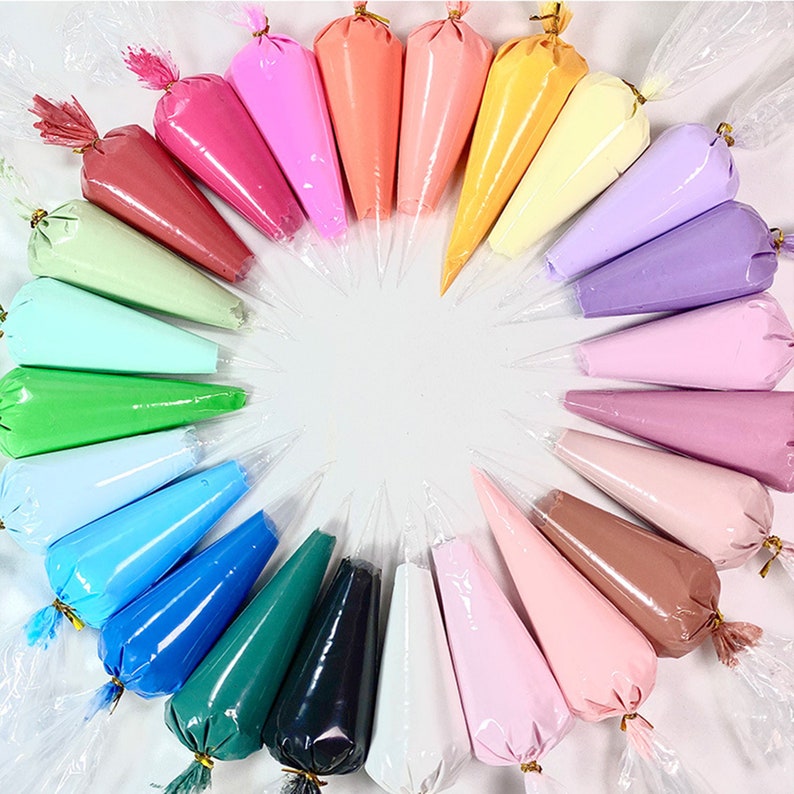 May include: A collection of colorful icing bags arranged in a circular pattern. The bags are filled with various shades of pink, red, green, blue, yellow, and brown. Each bag is sealed with a twist tie, ready for decorating cakes and other baked goods.