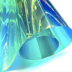 A sheet of iridescent film, displaying a spectrum of colors including blue, green, and yellow. The material is folded, creating a layered effect with varying shades and highlights. The overall appearance is smooth and reflective.