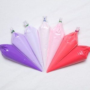 May include: Six pastry bags filled with colorful frosting in shades of purple, pink, and red. The bags are arranged in a fan shape, with the tips pointing towards the center. Each bag is sealed with a twist tie.