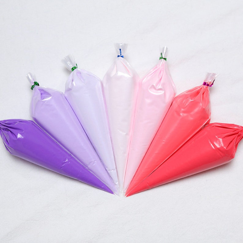 May include: Six pastry bags filled with colorful frosting in shades of purple, pink, and red. The bags are arranged in a fan shape, with the tips pointing towards the center. Each bag is sealed with a twist tie.