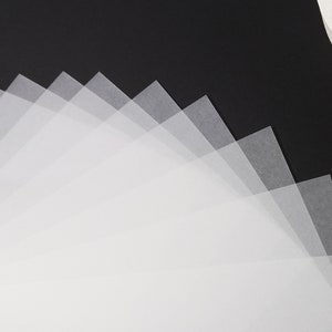 May include: A collection of translucent, square-shaped, white papers fanned out against a black background. The papers are layered, creating a gradient effect from light to dark. A white, circular object is in the upper right corner.