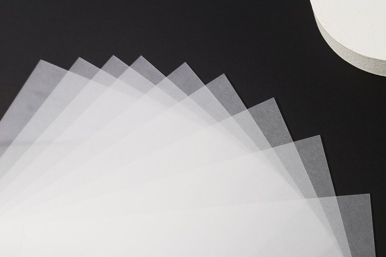 May include: A collection of translucent, square-shaped, white papers fanned out against a black background. The papers are layered, creating a gradient effect from light to dark. A white, circular object is in the upper right corner.