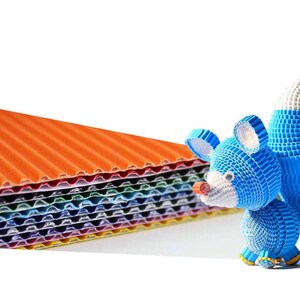 May include: A stack of colorful corrugated cardboard sheets with a blue papercraft animal figurine in the foreground. The animal is shaped like a fox with a long tail and a pointed snout.