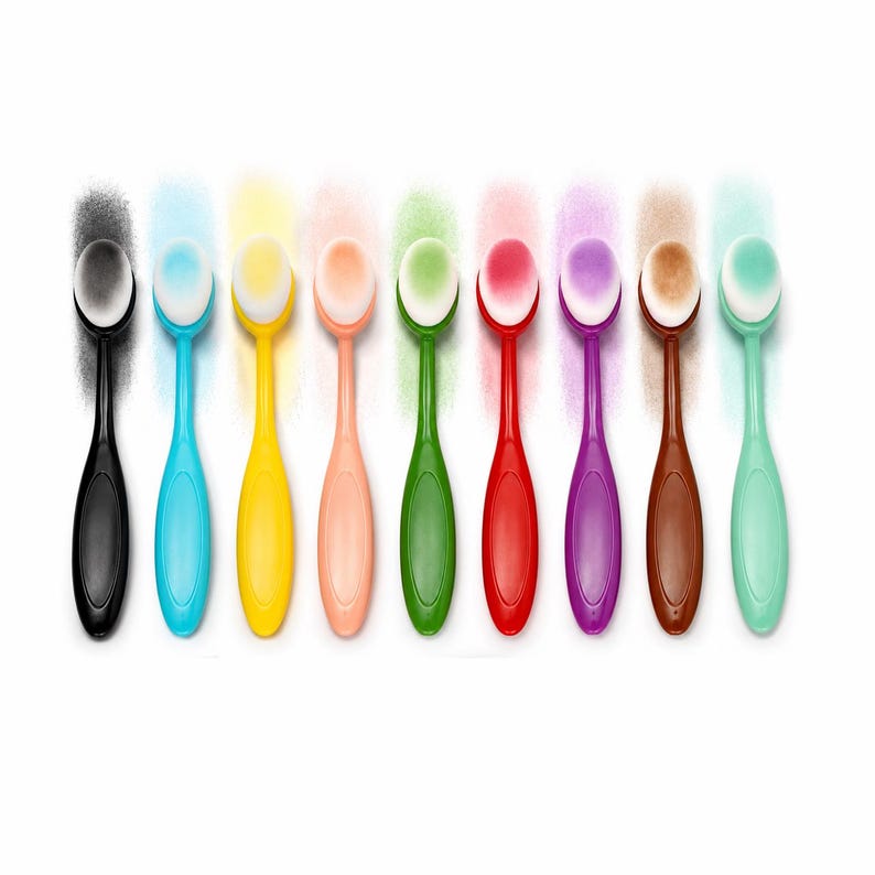 May include: A collection of nine oval-shaped makeup brushes with colorful handles and white bristles. Each brush has a different colored handle, including black, blue, yellow, peach, green, red, purple, brown, and mint green. The brushes are arranged in a row against a white background.