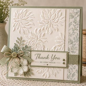 Peut inclure: Carte de vœux faite à la main avec un fond crème et une bordure vert sauge. La carte présente des motifs floraux en relief, un nœud décoratif et une étiquette avec l'inscription "Thank You". La carte est ornée d'un bouton et de feuilles.