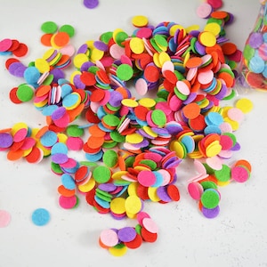 May include: A vibrant assortment of colorful felt circles in various sizes and shades, including red, orange, yellow, green, blue, and purple. These craft supplies are scattered across a white surface, suggesting a playful and creative theme.