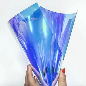 Pu&ograve; includere: Fogli di plastica flessibile blu e viola iridescenti. Il materiale &egrave; tenuto in mano. La superficie lucida e riflettente cambia colore a seconda della luce. Il materiale &egrave; traslucido.