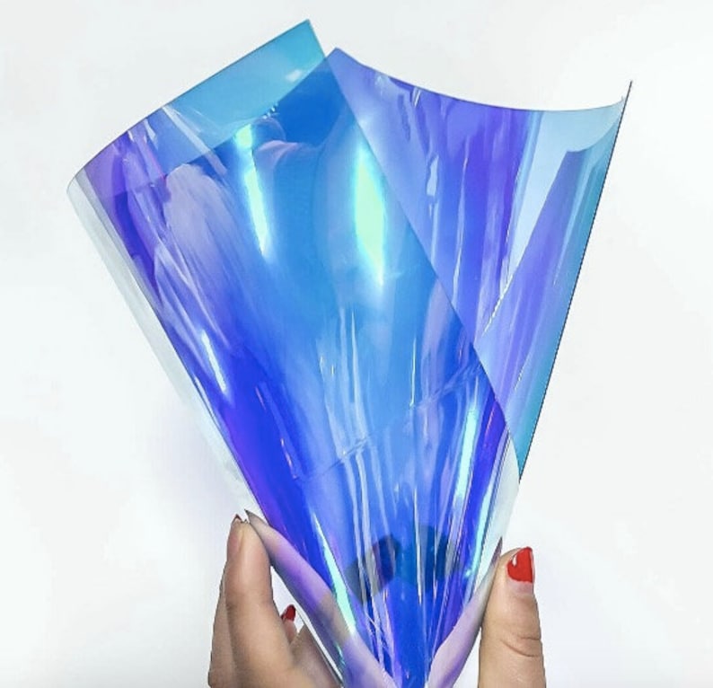 Pu&ograve; includere: Fogli di plastica flessibile blu e viola iridescenti. Il materiale &egrave; tenuto in mano. La superficie lucida e riflettente cambia colore a seconda della luce. Il materiale &egrave; traslucido.