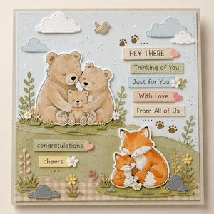 Può includere: Un biglietto di auguri con illustrazioni di orsi e volpi. Il biglietto include le frasi "Hey There", "Thinking of You", "Just for You", "With Love" e "From All of Us", insieme a "congratulations" e "cheers".