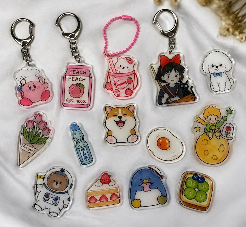 May include: A collection of clear acrylic keychains with various designs. The keychains feature cartoon characters, food items, and other cute illustrations. Some keychains have silver metal rings, while others have pink beaded chains.