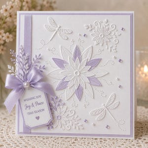 Puede incluir: Tarjeta de felicitación blanca con diseños florales y de libélulas en relieve, acentuada con lavanda. Una cinta y etiqueta lavanda con el texto "Wishing You Joy & Peace THIS SEASON" están adjuntas. La tarjeta tiene forma cuadrada.