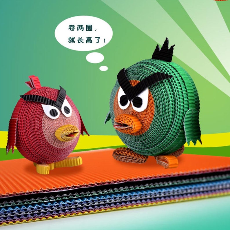 May include: Two cartoon birds made of colorful corrugated cardboard. The red bird is on the left and the green bird is on the right. The green bird has a thought bubble above its head with the text "老两圈, 就长高了!" in Chinese characters. The birds are sitting on a stack of corrugated cardboard sheets in various colors.