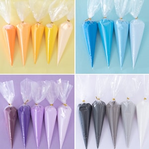 May include: A collection of colorful piping bags filled with frosting. The bags are arranged in rows, showcasing a variety of hues including orange, yellow, blue, purple, gray, and white. Each bag is sealed with a twist tie.