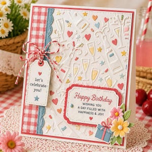 May include: A handmade birthday card with a white embossed background featuring champagne bottles, glasses, hearts, and stars. The card includes a tag that says "let's celebrate you!" and a message that says "Happy Birthday". Decorative flowers and a gift box are attached.