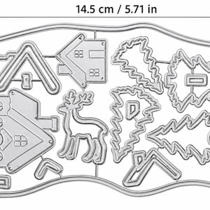 Op de afbeelding: Een zilverkleurige metalen snijmalset met contouren van huizen, een rendier en dennenbomen. De set meet 14,5 cm in de breedte en 9 cm in de hoogte, waarbij de verschillende vormen verbonden zijn door dunne metalen verbindingsstukjes.