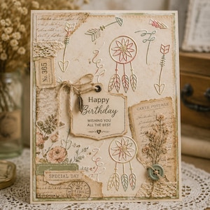 Op de afbeelding: Handgemaakte verjaardagskaart met een vintage uitstraling. De kaart heeft pijlen, dromenvangers, bloemmotieven en de tekst "Happy Birthday, Wishing You All The Best". Een knoop en touw voegen details toe.