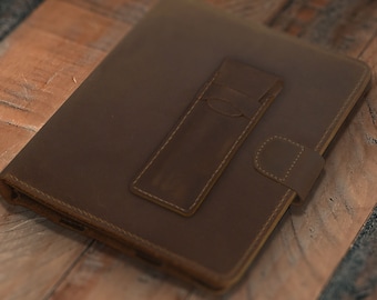May include: A brown leather journal with a pen holder and a snap closure. The journal is rectangular and has a textured surface. The pen holder is attached to the front of the journal with white stitching.