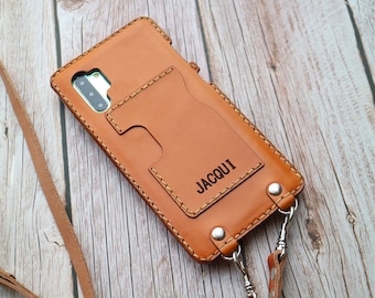 May include: A brown leather phone case with a card slot and a strap. The case has the word "JACQUI" embossed on the back.
