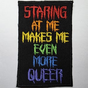 Peut inclure: Écusson rectangulaire noir avec texte brodé aux couleurs de l'arc-en-ciel. Le texte se lit comme suit : "STARING AT ME MAKES ME EVEN MORE QUEER". L'écusson a une bordure noire et est conçu pour être cousu ou repassé sur des vêtements ou des accessoires.