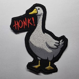 May include: Embroidered patch of a goose with grey and white feathers, yellow feet, and a yellow beak. The goose has a black outline and a speech bubble that says "HONK!" in red letters.