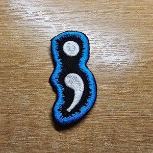 May include: Blue and white embroidered patch in the shape of a semicolon.